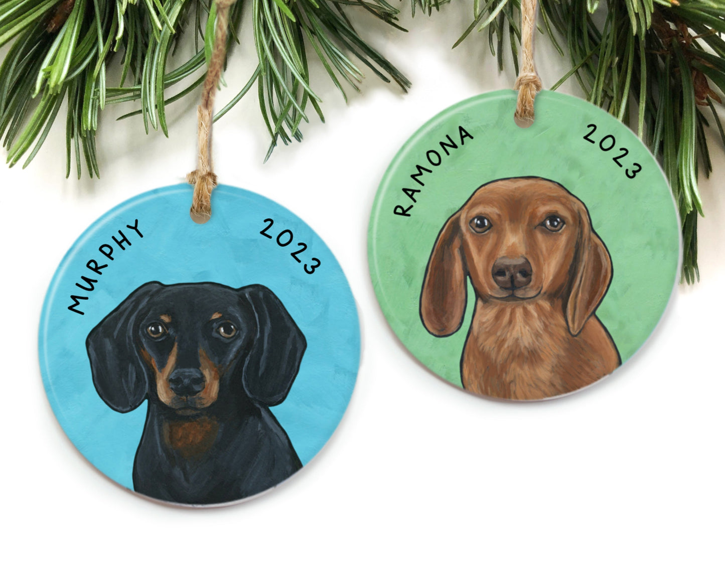 Two custom pet portrait ornaments hanging from pine needles. One black and tan dachshund, one brown dachshund