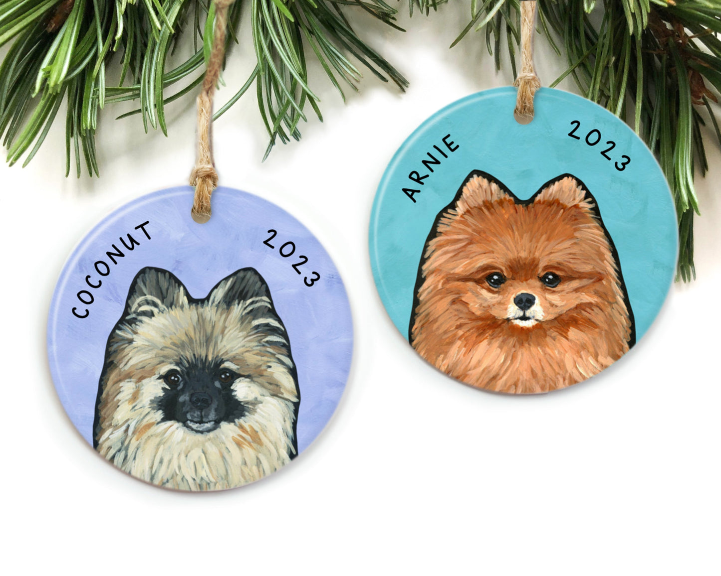 Two Pomeranian ornaments by The Cheery Pet (Jessi McNeal) hanging from pine needles