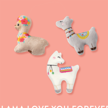 Three llama plush toys, one cream with flowers, one grey with a blanket, and one white with a blanket
