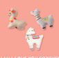 Three llama plush toys, one cream with flowers, one grey with a blanket, and one white with a blanket