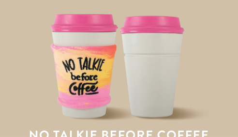 Two white coffee cups with pink lids, one with a colorful sleeve that says No Talkie Before Coffee