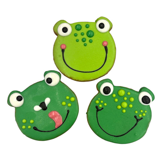 Three green frog-shaped cookies with different facial expressions